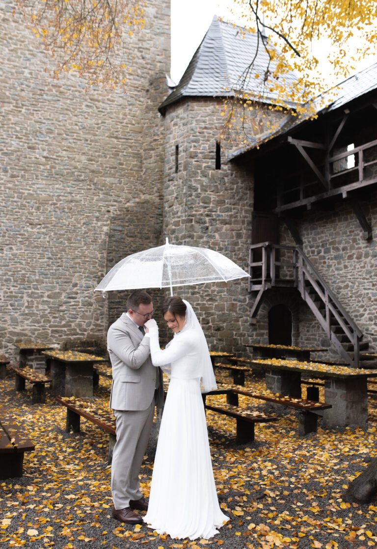 Brautpaar mit Regenschirm im herbstlichen Burghof – Hochzeit bei Regen