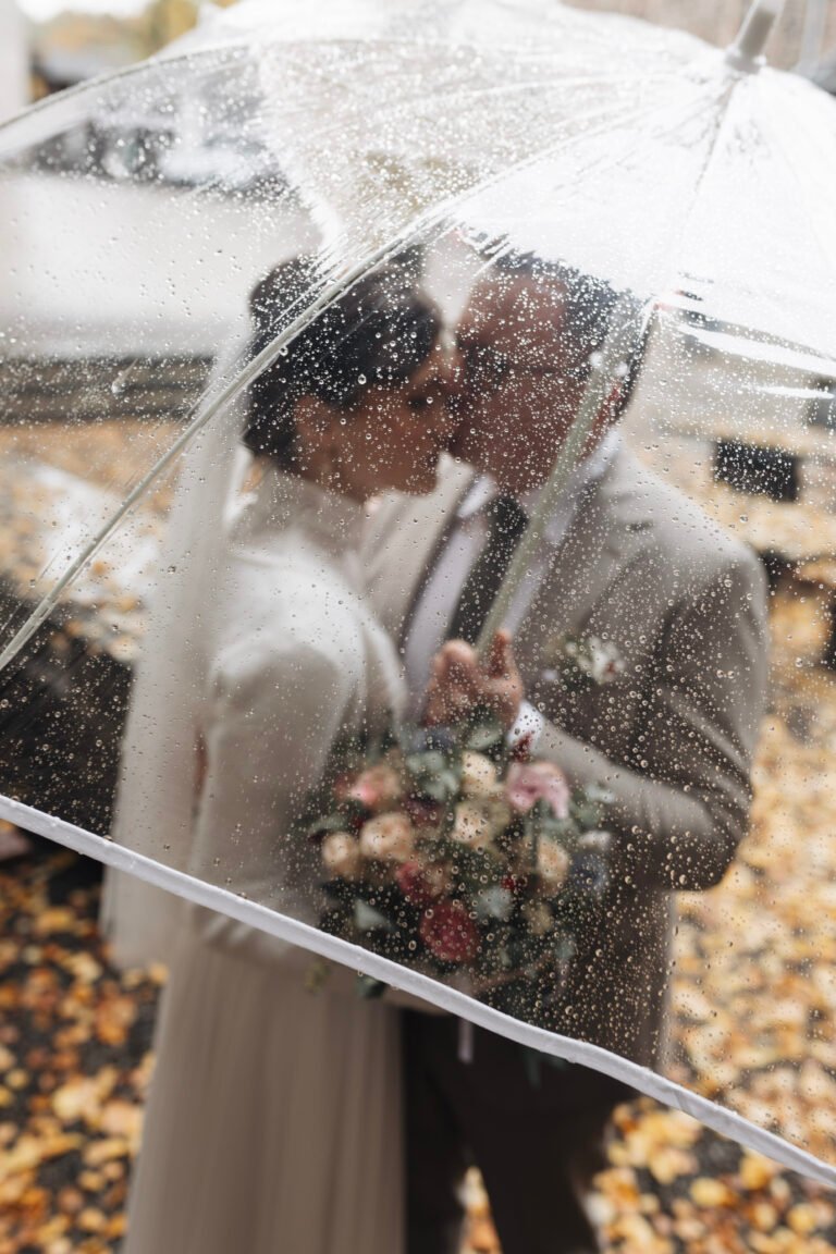Brautpaar küsst sich unter einem Regenschirm voller Regentropfen