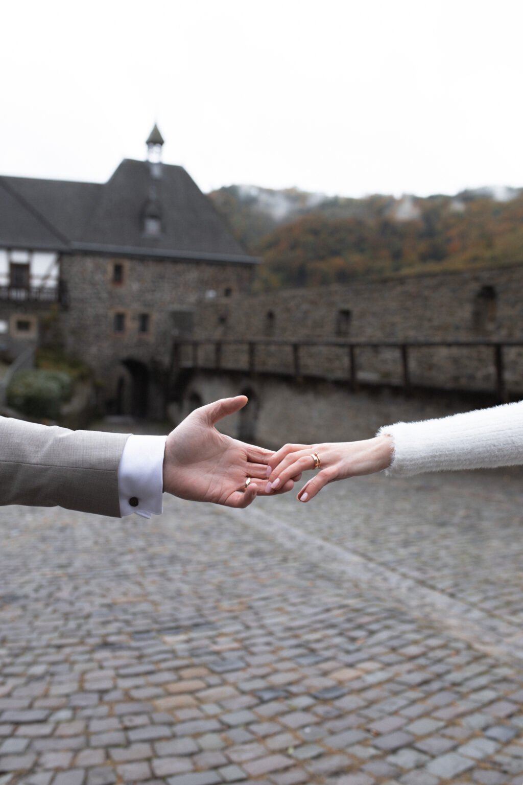 Hände des Brautpaares berühren sich vor historischer Burgkulisse – Hochzeitsfotografie von Aydin Genn