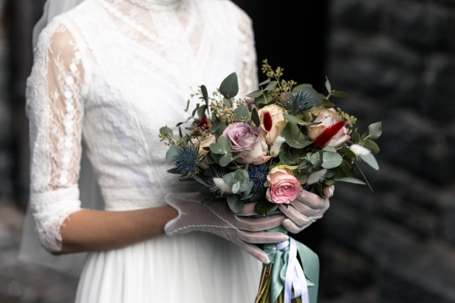 Braut mit Spitzenhandschuhen hält einen Brautstrauß aus Rosen und Eukalyptus