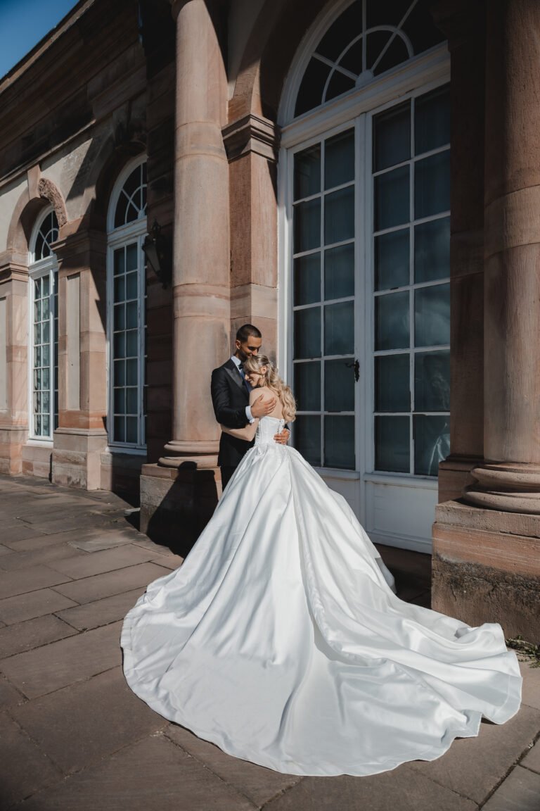 Braut mit langer Schleppe vor historischer Schlossfassade